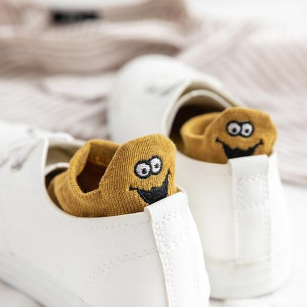 Mustard ankle socks with embroidered smiling character peeking out of white trainers