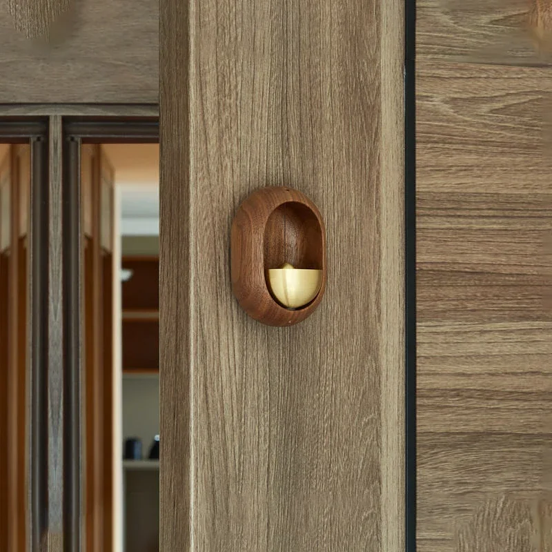 Brown wood-effect oval door bell with gold-tone bell beside a wooden door