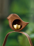 Brown wood-effect bird door bell with gold-tone bell against a green blurred background
