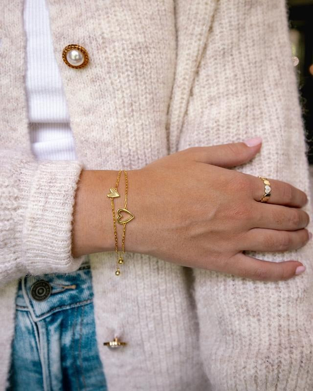 Gold-tone adjustable heart bracelets layered on a wrist with a cream knit cardigan