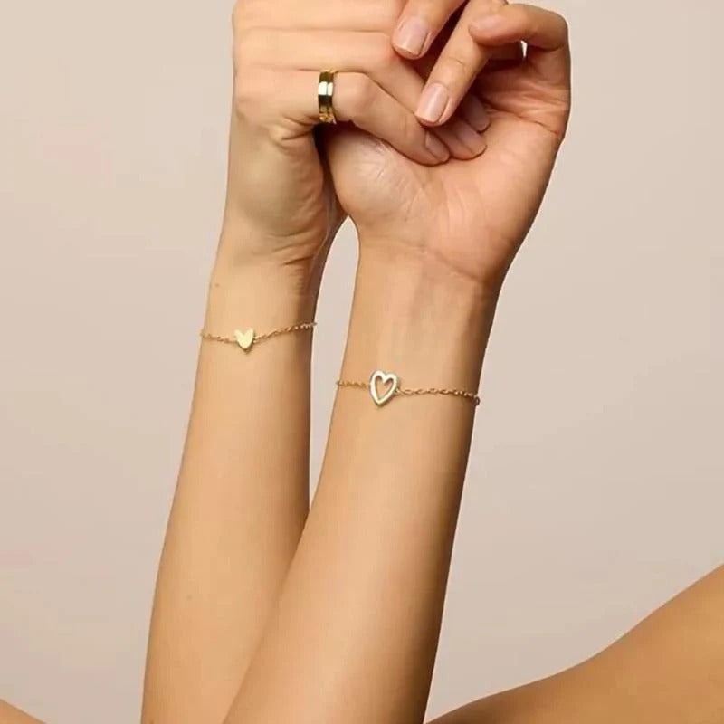 Gold-tone heart bracelets worn on two wrists with hands clasped