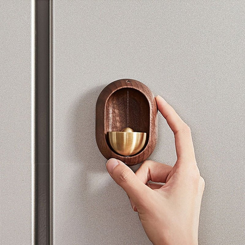 Hand holding a brown wood-effect oval door bell with gold-tone bell against a grey wall