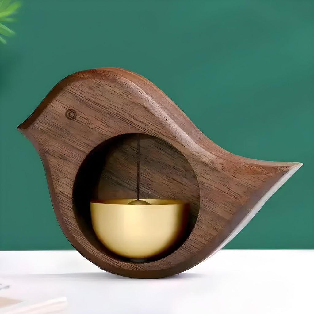 Wood-effect bird door bell with gold-tone bell on a white surface against a green backdrop