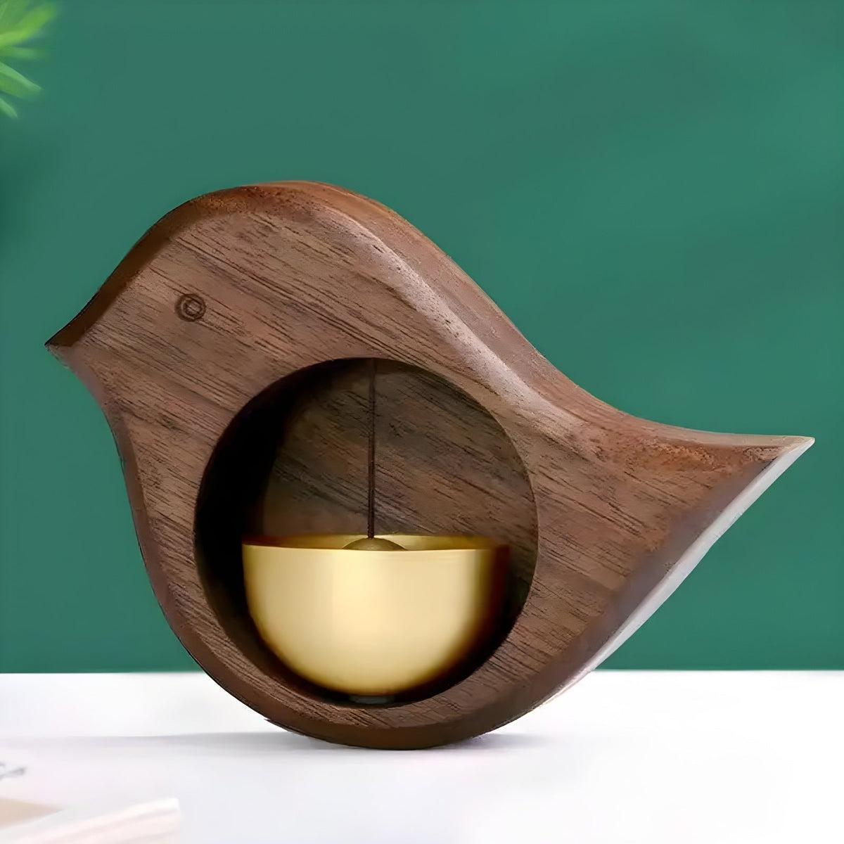 Wood-effect bird door bell with gold-tone bell on a white surface against a green backdrop