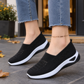 Black breathable knit slip-on sneakers for women with ventilated panels and white raised sole, worn with frayed-hem jeans