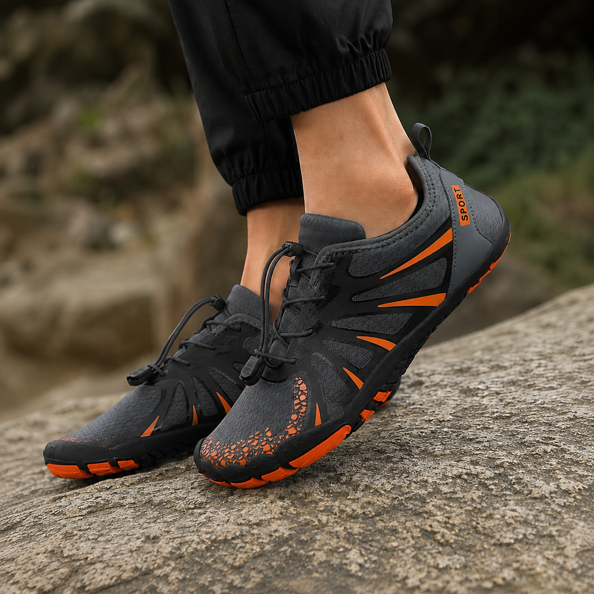 Barefoot water shoes for women in dark grey with orange accents, worn on a rock