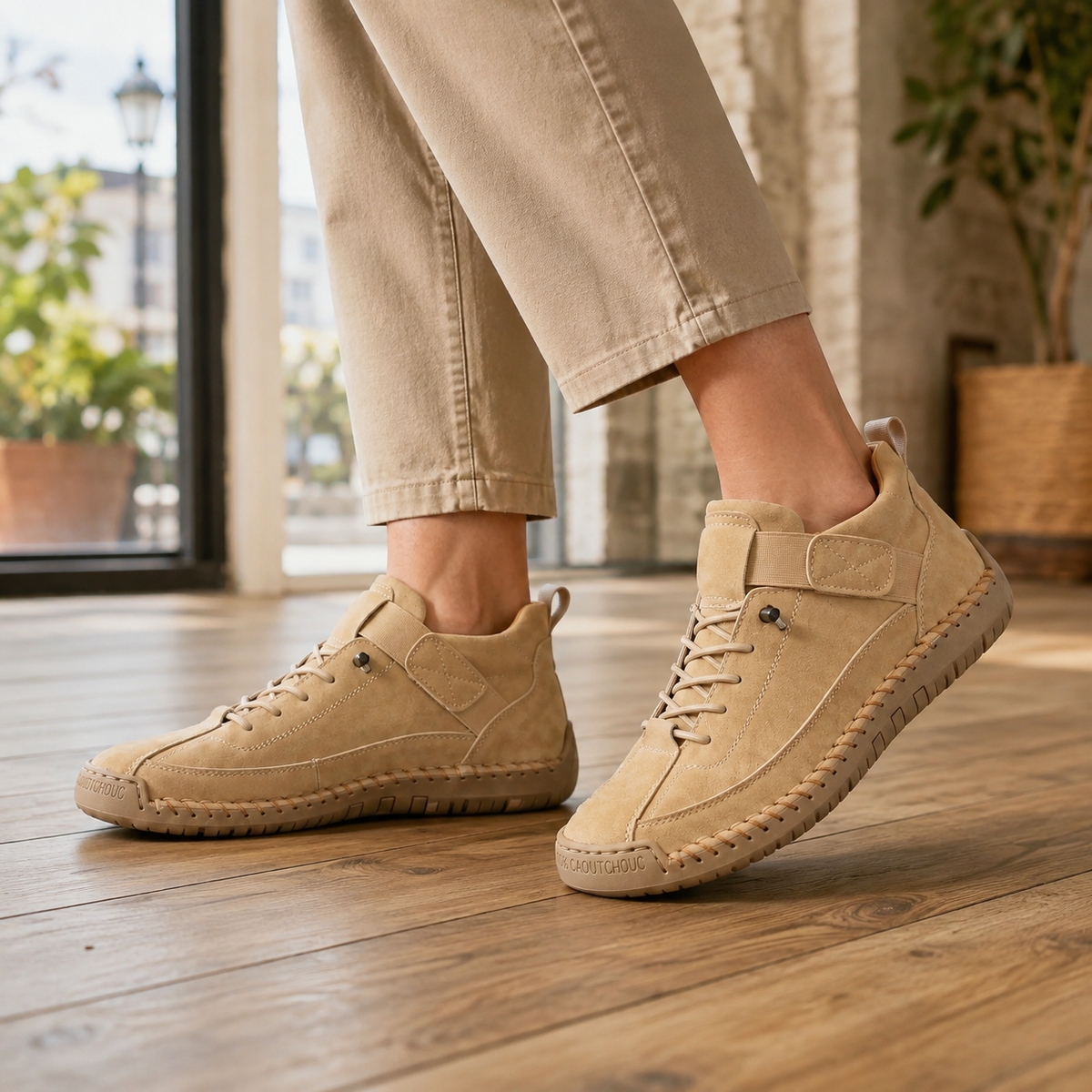 Beige leather orthopedic sneakers for women with elastic lace-up closure, instep strap and stitched sole edge, worn with khaki trousers on a wooden floor.
