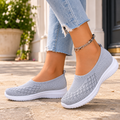 Grey orthopedic sneakers for women with a white sole, worn with jeans on a stone pavement.