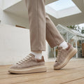 Platform sneakers women can wear with beige trousers: apricot taupe suede with a brown heel tab, wide flat laces and a chunky cream sole.