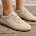 Beige suede sneakers with gum sole, front three-quarter view worn on a wooden boardwalk by the sea