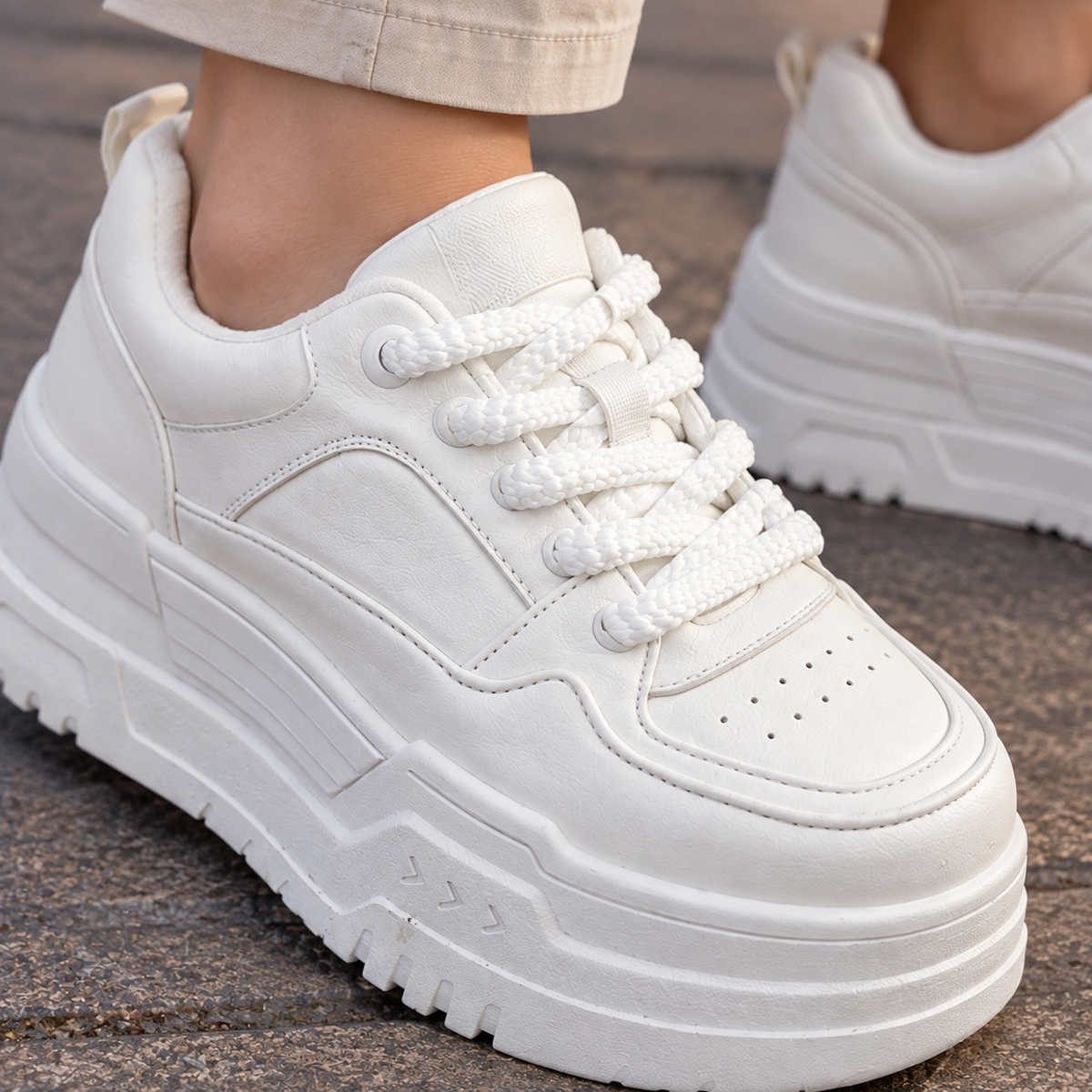 Close-up of a white chunky platform trainer with thick braided laces, perforated toe and textured sole