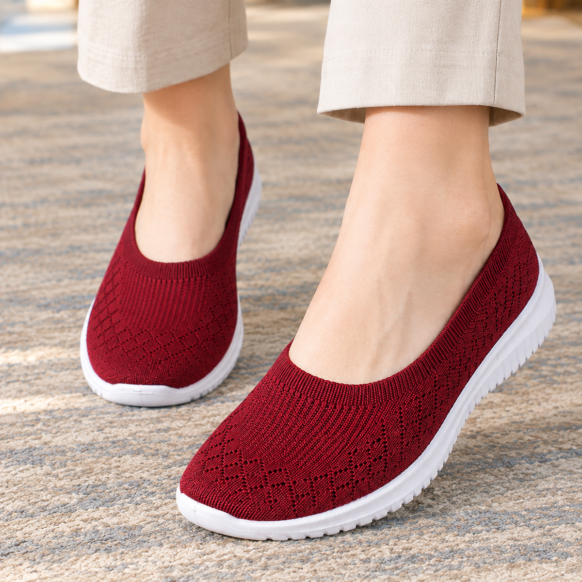 Close-up of the red knitted slip on trainers with a white sole, worn with beige trousers.