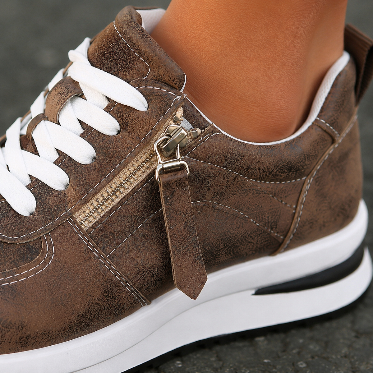 Close-up of brown platform trainers showing the side zip, laces and layered sole