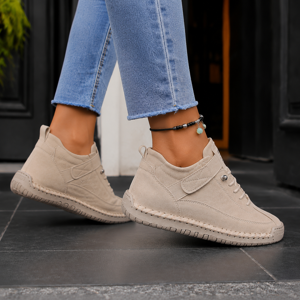 Side view of beige sneakers with strap and stitched sole, worn mid-step with light jeans.