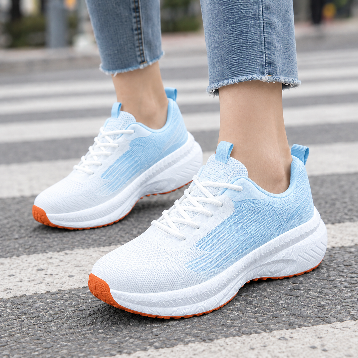 White and light blue mesh knit lace-up trainers with thick white platform sole and orange outsole, worn with frayed jeans
