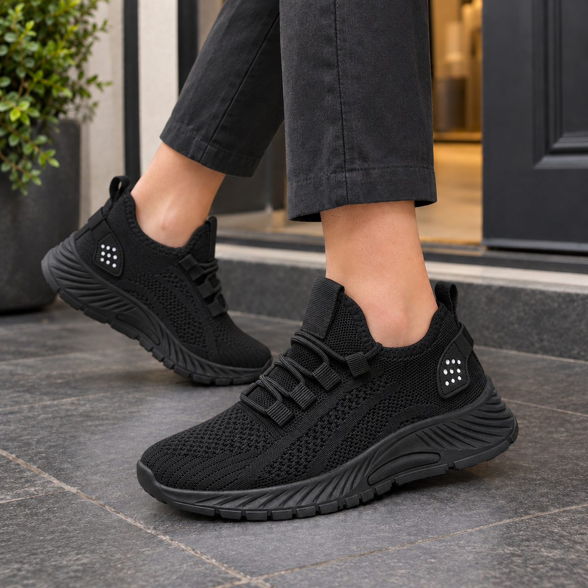 Black knitted mesh trainers with a platform sole, worn on a grey pavement.