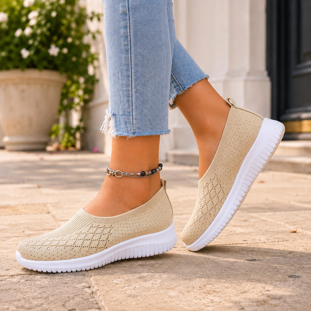 Cream knitted slip on trainers with a white sole, worn with jeans on a stone pavement.