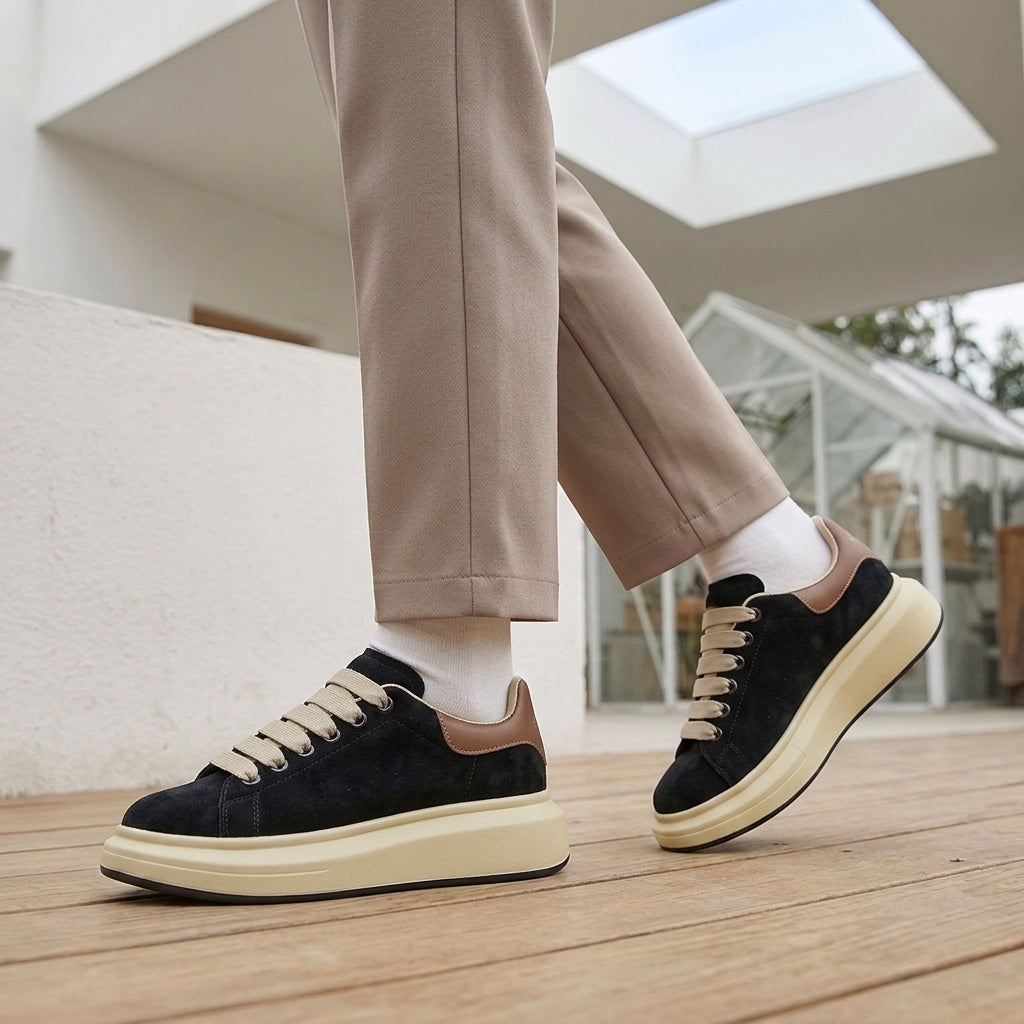 Black suede platform sneakers with a brown heel tab, beige flat laces and a chunky cream sole.