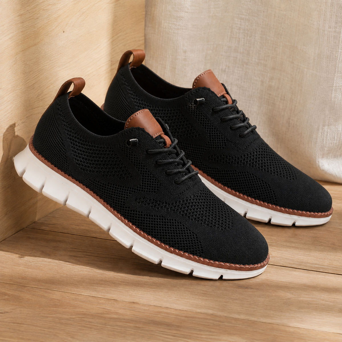 Pair of black knit lace-up sneakers with a white ridged sole, angled view on a wooden floor
