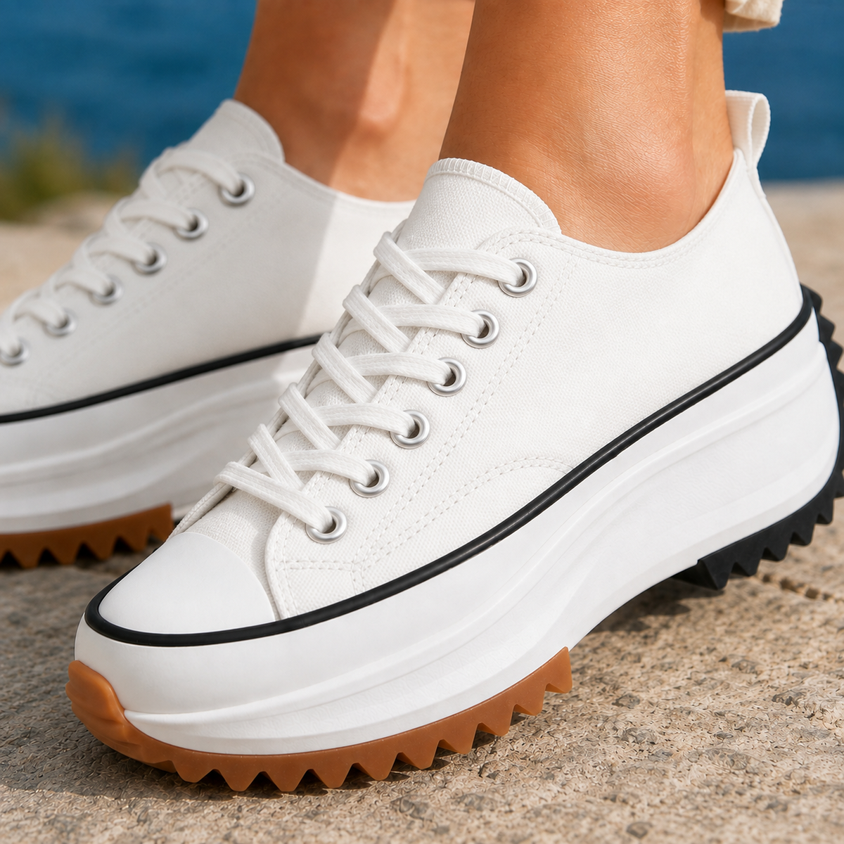 White woven platform sneakers with black line trim, white laces and a chunky sole with gum-coloured tread, worn by the sea