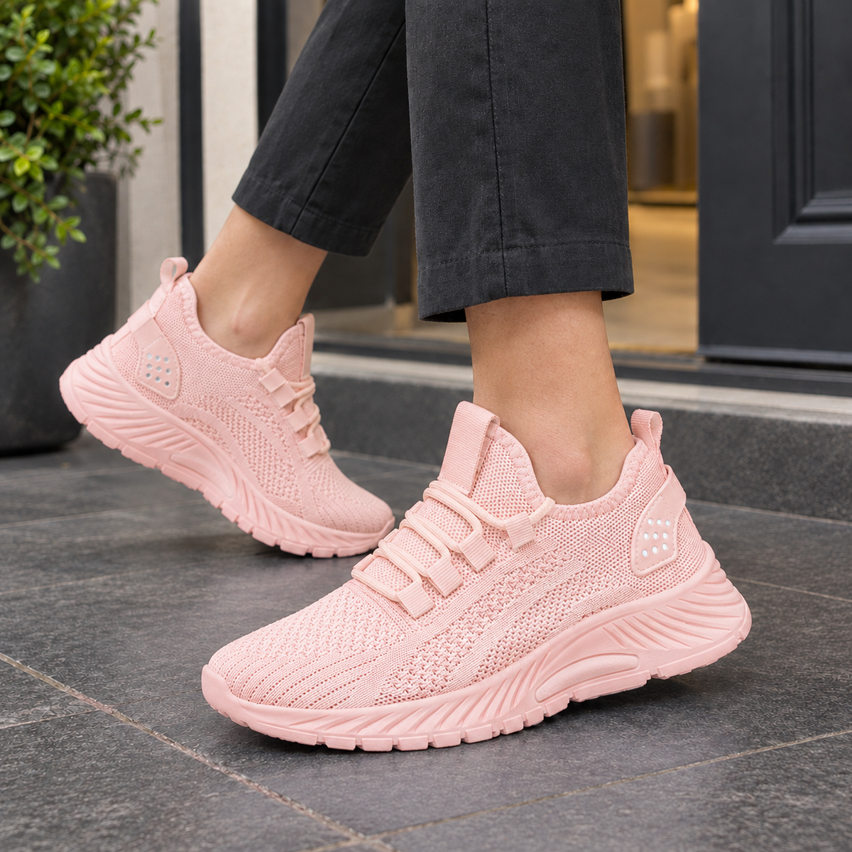 Pink knitted mesh trainers with a platform sole, worn with black trousers on a grey pavement.