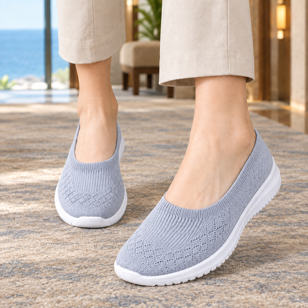 Grey knitted slip on trainers with a white sole, worn with beige trousers on a rug.