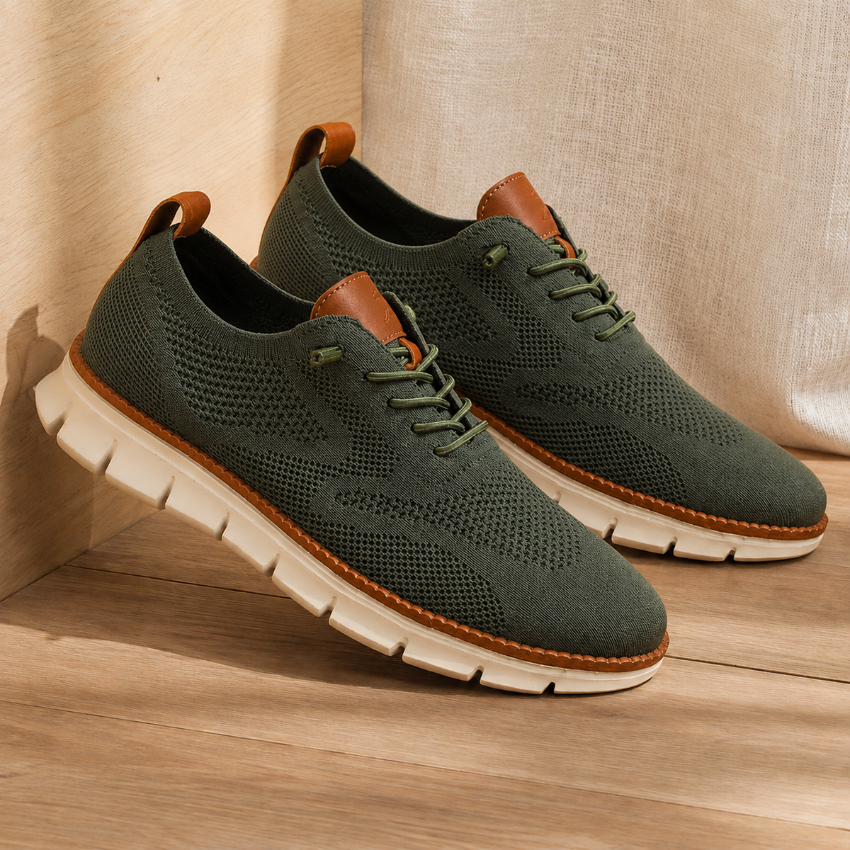 Pair of olive green knit sneakers with a cream ridged sole, angled view on a wooden floor