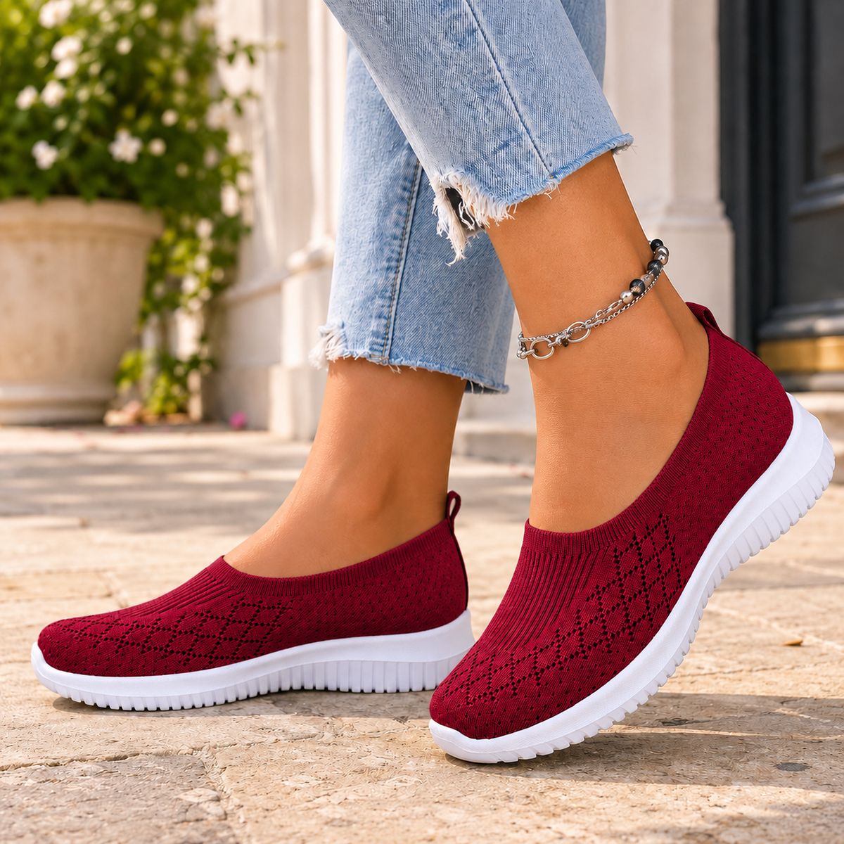 Red knitted slip on trainers with a white sole, worn with jeans on a stone pavement.