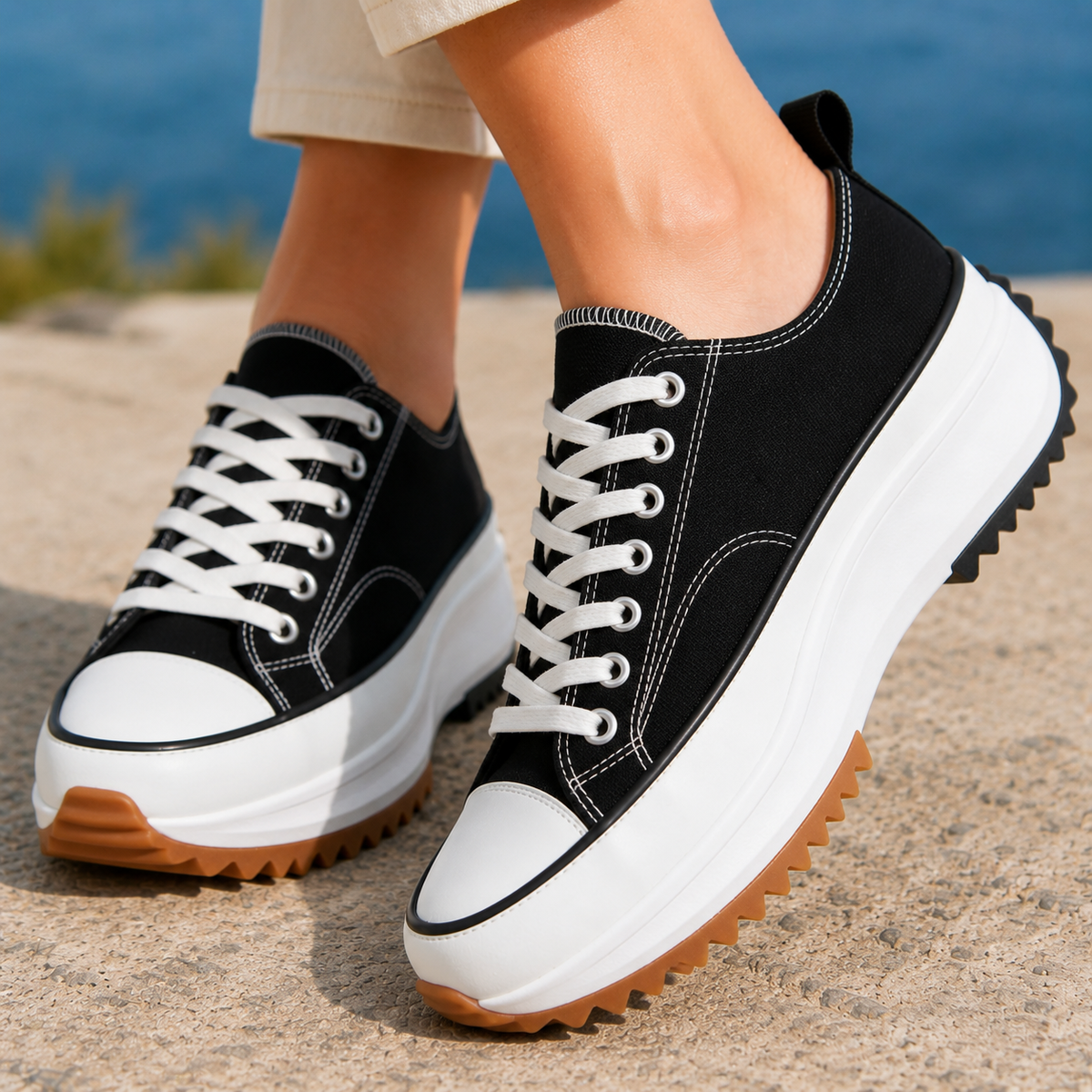 Black woven platform trainers with white laces and stitching, a contrast toe cap and a chunky white sole, worn on a sandy ledge