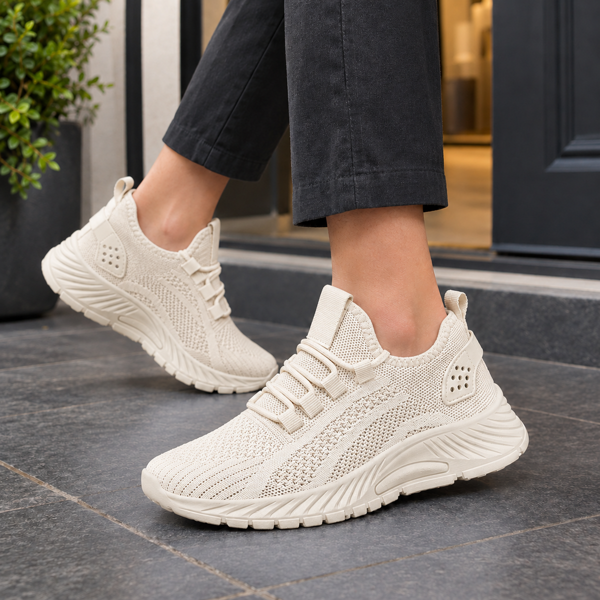 Beige knitted mesh trainers with a platform sole, worn with black trousers on a grey pavement.