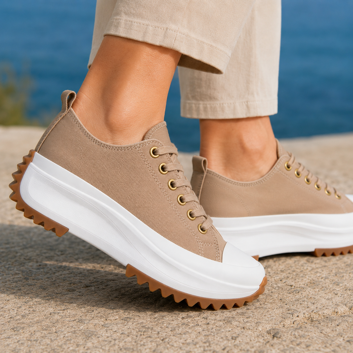 Tan woven platform trainers with gold-tone eyelets, tonal laces and a chunky white sole, worn with beige trousers by the sea
