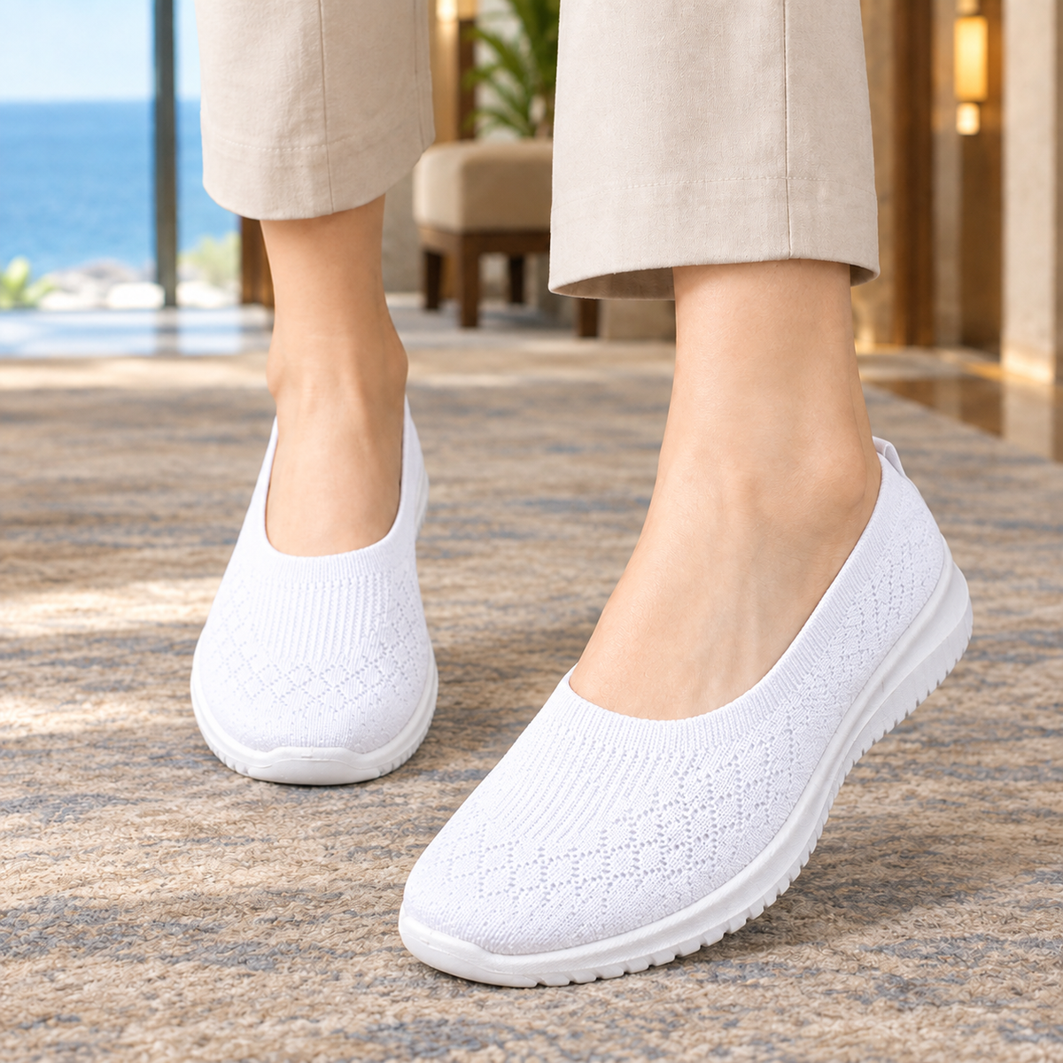 White knitted slip on trainers with a white sole, worn with beige trousers on a rug.