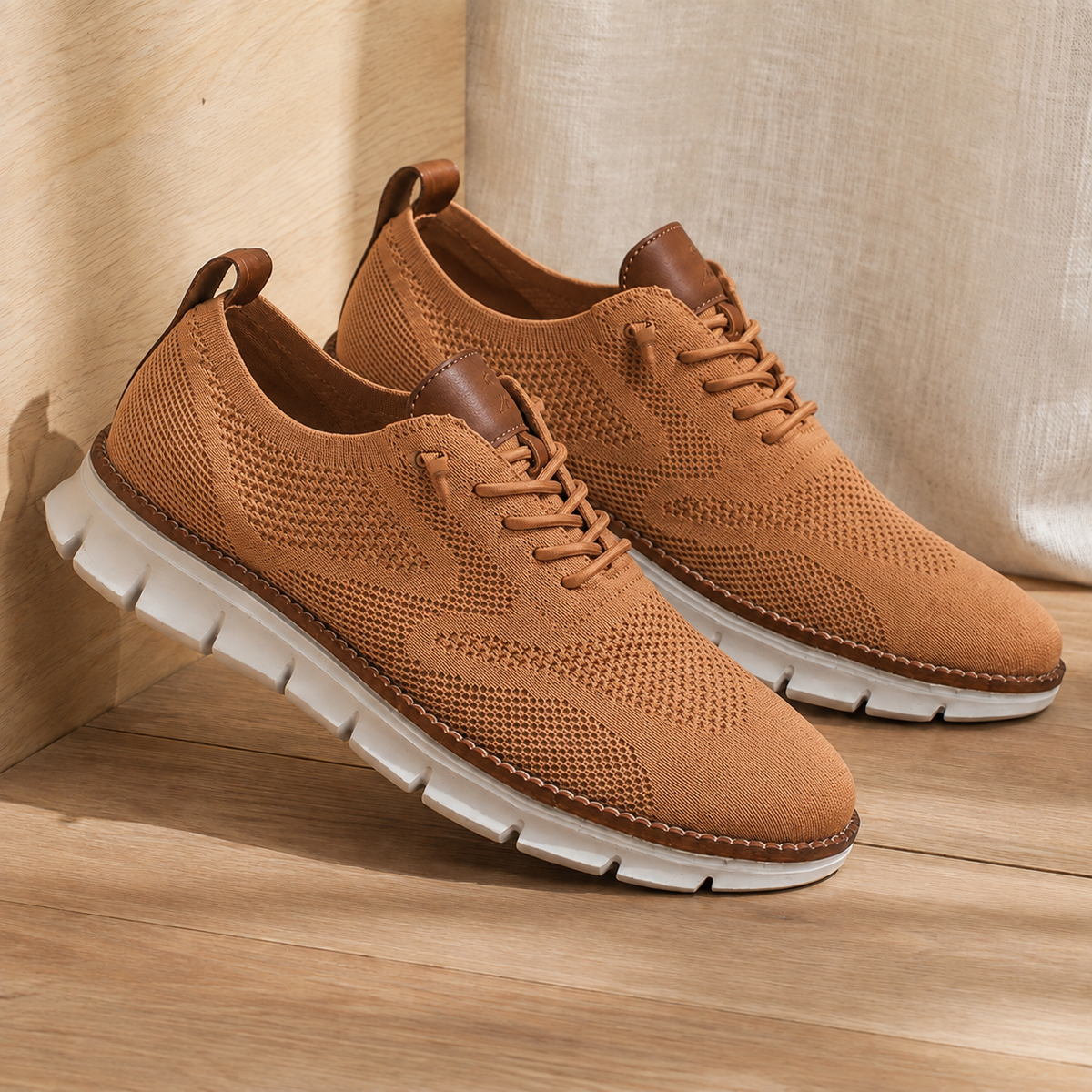 Pair of caramel knit sneakers with a white ridged sole, angled view on a wooden floor