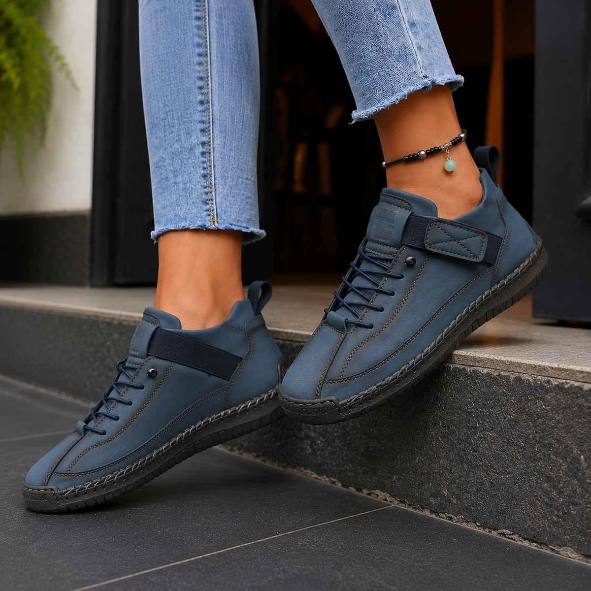 Dark blue lace-up sneakers with elastic strap and dark stitched sole, worn mid-step on a stone step.