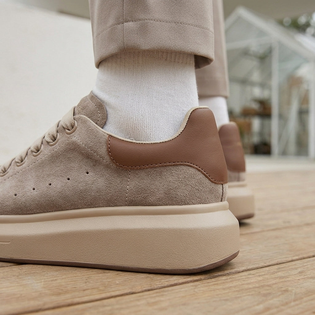 Close-up of the heel of apricot taupe suede platform sneakers with a brown leather heel tab and perforations.