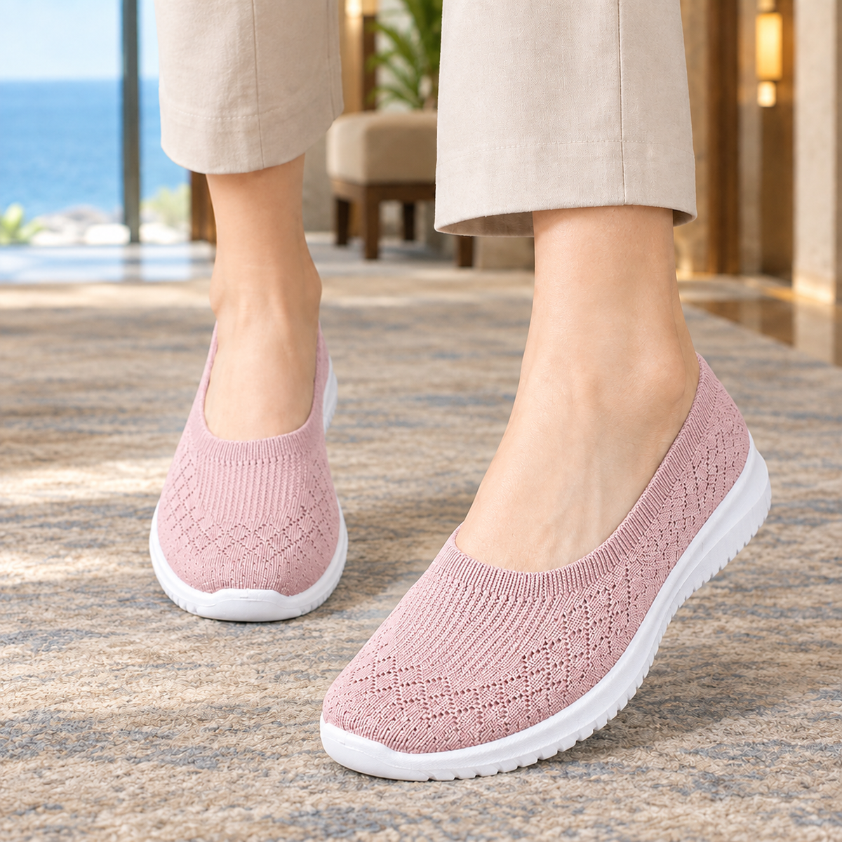 Pink knitted slip on trainers with a white sole, worn with beige trousers on a rug.
