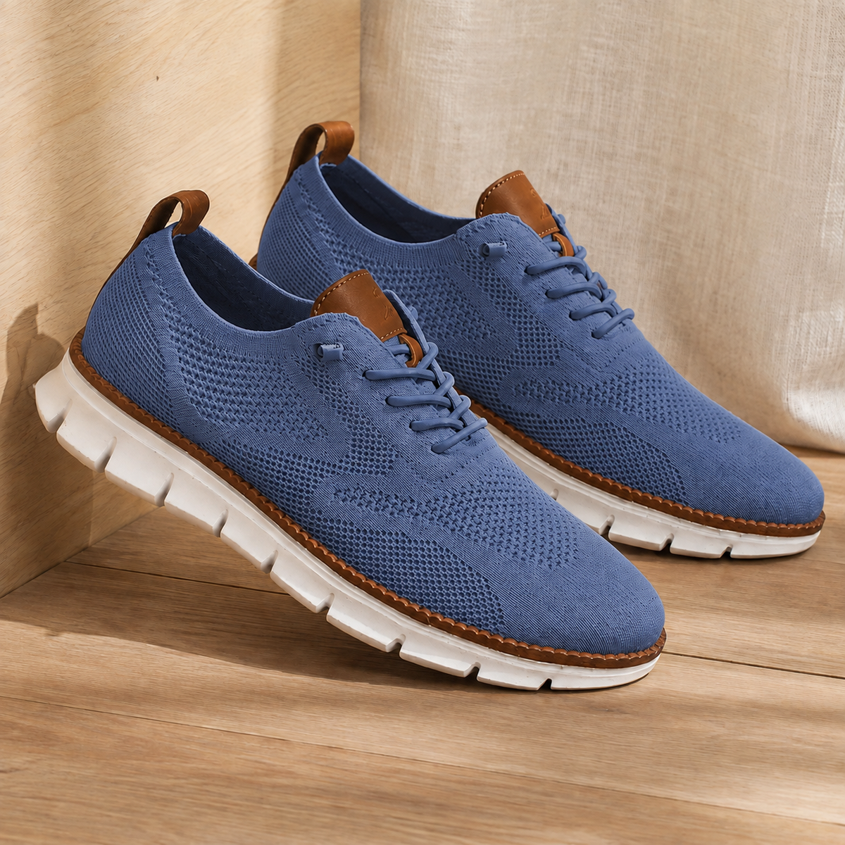 Pair of blue knit sneakers with a white ridged sole, angled view on a wooden floor