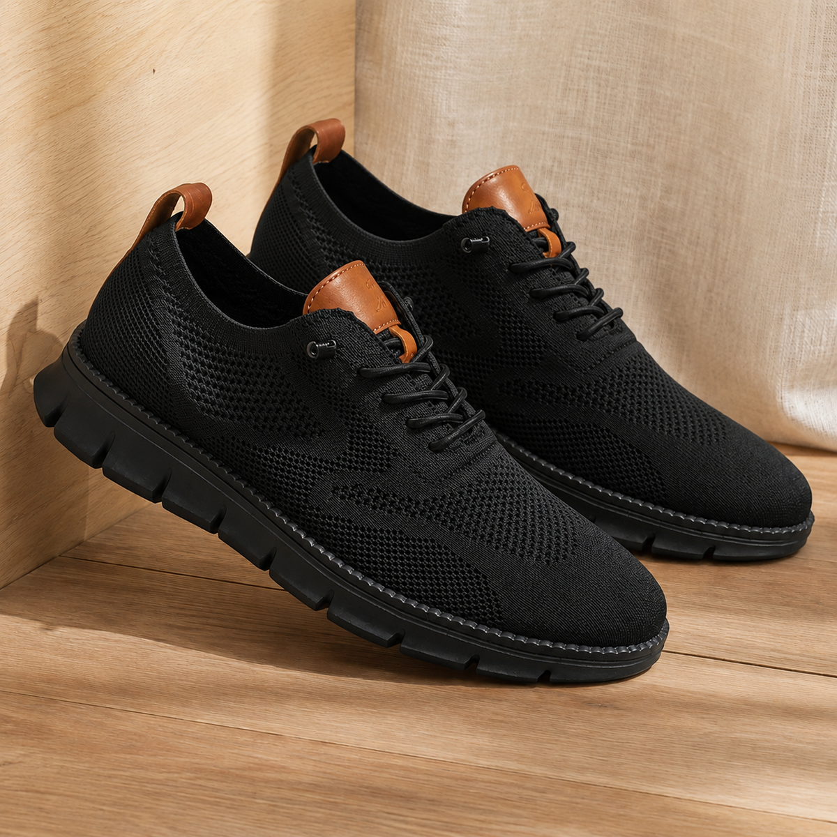 Pair of all-black knit sneakers with a black sole, angled view on a wooden floor