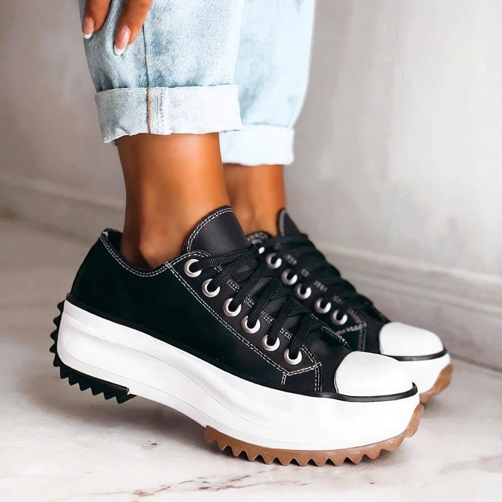 Women's platform trainers in black with a white chunky platform sole, shown worn with rolled jeans